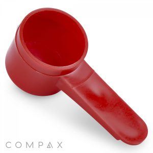 A red plastic 6.5cc Scoop featuring a cylindrical measuring cup and a short, flat handle angled slightly upward. The background is white, and the brand name "COMPAX" is visible at the bottom left corner.