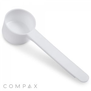 A white, plastic 18cc scoop featuring a cylindrical bowl and a long, straight handle designed for precise measurements. The brand name "COMPAX" is displayed in grey text in the lower-left corner of the image.