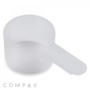 A 20cc Scoop made of clear plastic, featuring a rounded body and a flat, elongated handle, is set against a plain white background. The brand name "Compax" is partially visible at the bottom right corner.