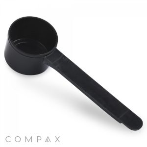 On a plain white background, a 20cc Scoop made of black plastic with a long handle is placed. The scoop features a cylindrical measuring cup at one end, and the brand name "COMPAX" is clearly visible in the bottom left corner.