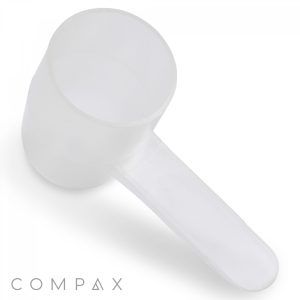 A transparent 2cc measuring scoop with an extended handle is displayed against a white background, featuring the brand name "COMPAX" in the bottom left corner of the image.