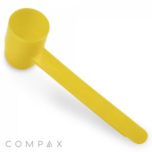 A 2cc Scoop made of yellow plastic with a long handle is positioned diagonally across a white background. The branding "COMPAX" is prominently displayed in the bottom left corner.