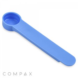A blue plastic 1cc scoop with the word "TEASPOON" embossed in the circular measuring area. The scoop is long and flat with a rounded end for scooping. The logo "COMPAX" is visible in the bottom left corner of the image.