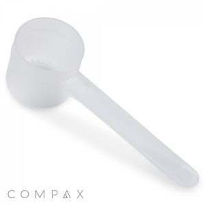 A clear plastic 26.5cc scoop with a long handle, photographed against a white background. The brand name "COMPAX" is written in subtle text at the bottom left corner.