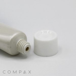 A close-up image of an uncapped, white plastic tube labeled "16mm Screw Top" lying on a flat surface. The screw-top cap is placed beside the tube. The background is plain white. The word "COMPAX" is faintly visible in the lower left corner.