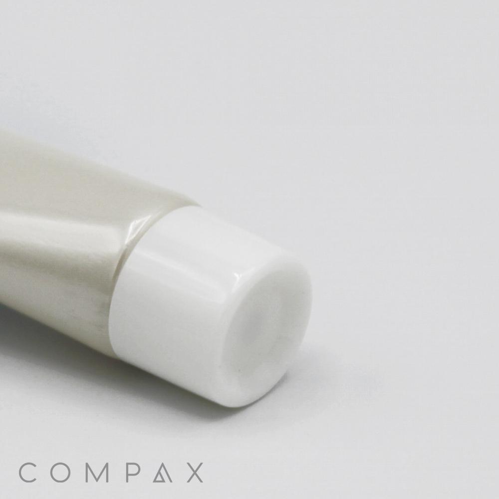 A 16mm Screw Top tube with a white cap is partially visible against a light grey background. The embossed text "COMPAX" appears in the bottom-left corner of the image. The tube is angled slightly to the left, and the image focuses on the cap end.