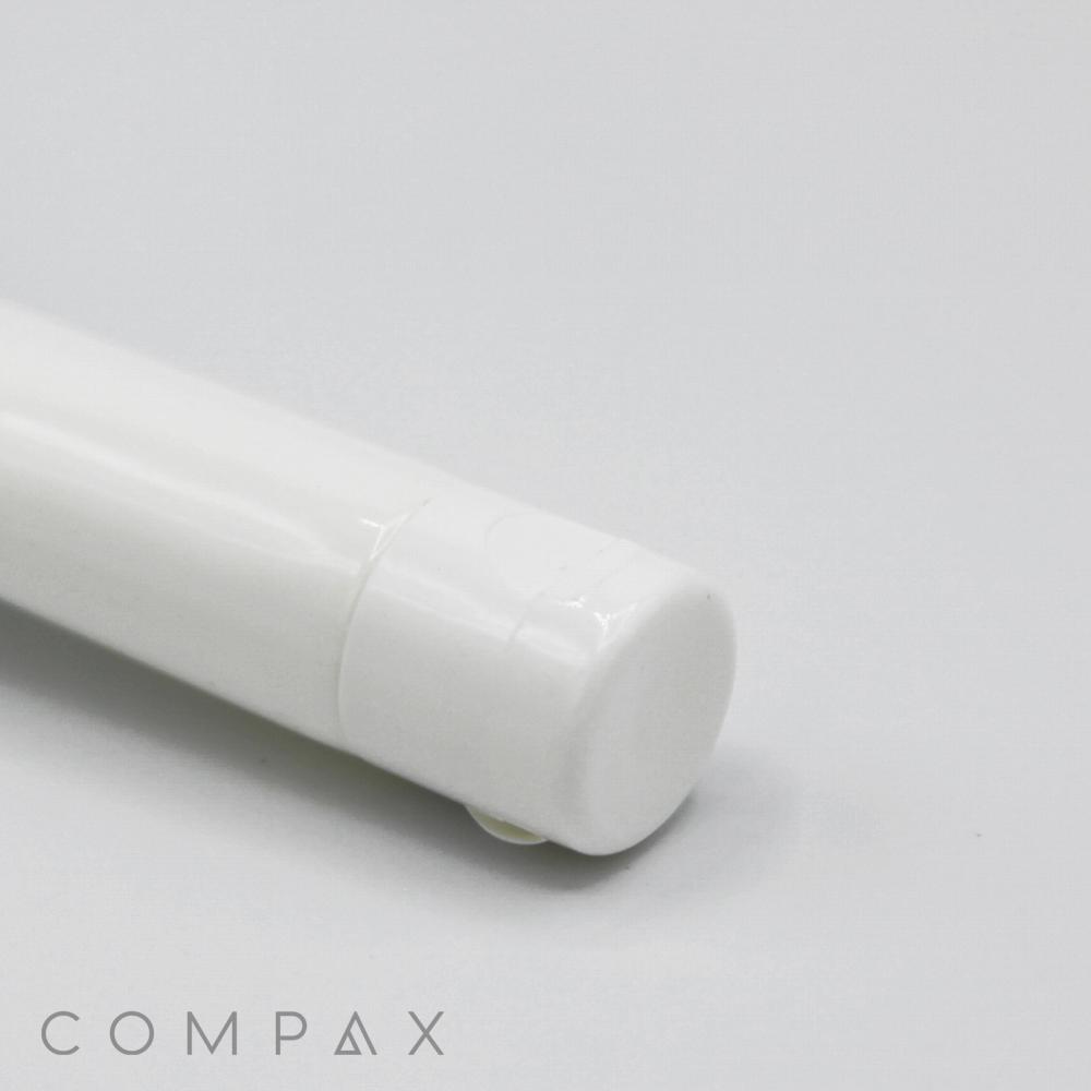 Close-up of a white cylindrical object, possibly the 16mm Flip Top, with the word "COMPAX" partially visible in the bottom left corner. The focus is on the cap end, and the background is light grey.