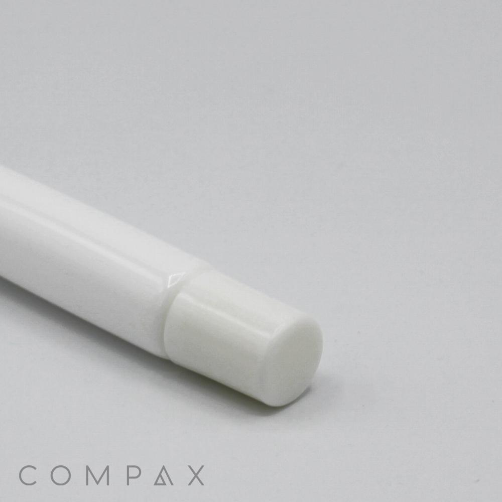 Close-up of the bottom end of a white 13mm Lip Applicator with a round cap placed on a light gray surface. The word "COMPAX" is subtly visible in lowercase letters near the bottom left corner of the image.