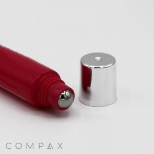A red 19mm Roller cosmetic tube with a metal rollerball applicator is shown with its shiny silver cap removed and placed next to it. The brand name "COMPAX" is visible at the bottom left corner of the image. The background is plain white.