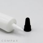 A "19mm Needle Nose Snip Tip" white plastic tube with a pointed tip dispenser is lying horizontally with its black cap removed and placed nearby on a white surface. The brand name "COMPAX" is visible in the bottom left corner.