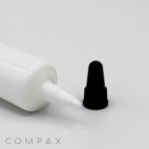 A "19mm Needle Nose Snip Tip" white plastic tube with a pointed tip dispenser is lying horizontally with its black cap removed and placed nearby on a white surface. The brand name "COMPAX" is visible in the bottom left corner.