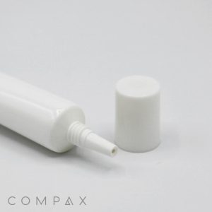 A white plastic 19mm Needle Nose squeeze tube with a narrow nozzle and a detached cap lying next to it on a plain white background. The word "COMPAX" is displayed at the bottom left corner.