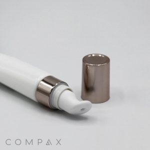 A close-up image of the 19mm Lip Applicator with a white body and metallic-finished applicator and cap, lying on a flat surface. The cap is removed and placed beside the tube. The brand name "COMPAX" is visible in the bottom-left corner of the image.