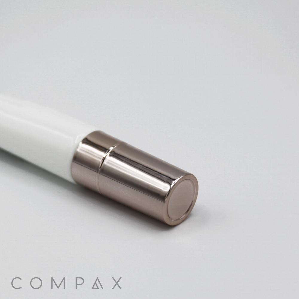 A close-up image of a sleek, white and silver 19mm Lip Applicator lying on a light gray surface. The cap is silver with a smooth, shiny appearance. The word "COMPAX" is displayed in light gray capital letters at the bottom left corner of the image.