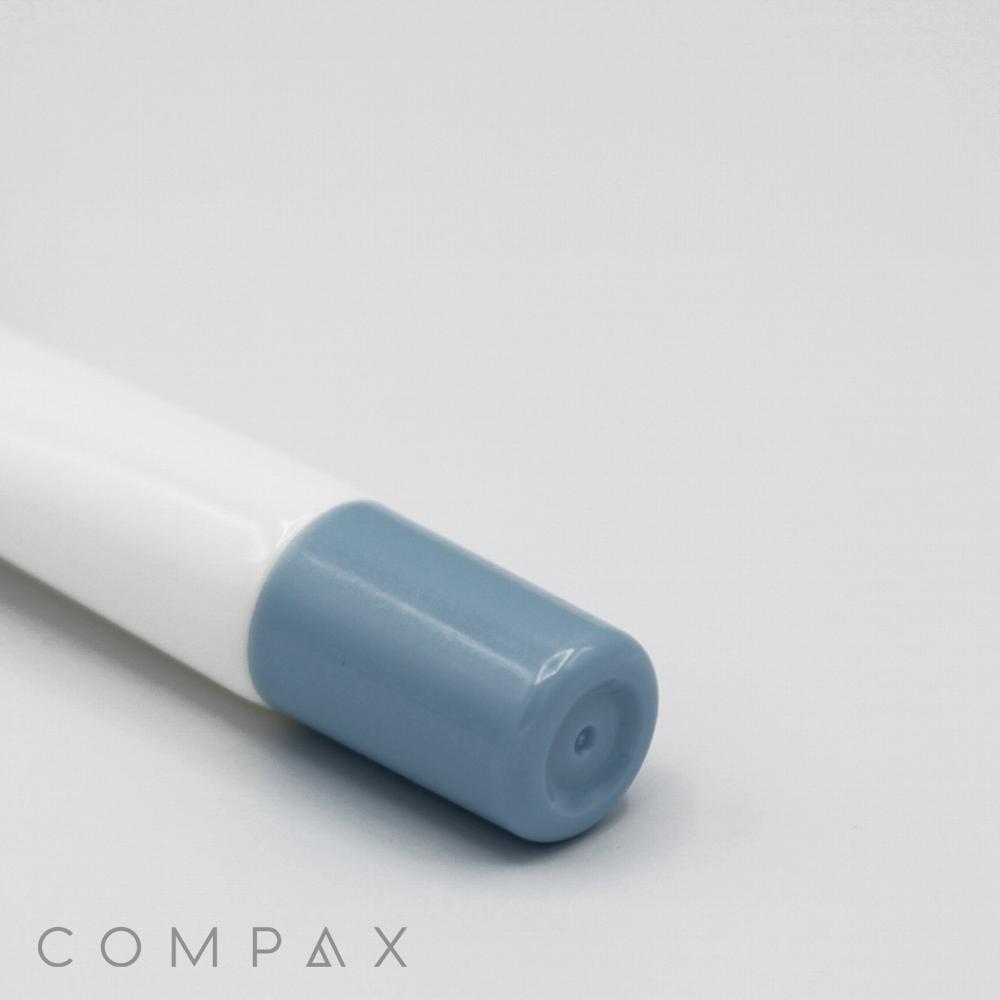 A 19mm Needle Nose pen with a light blue cap lies flat on a clean, light gray surface. The pen is branded with "COMPAX" in sleek, minimalist text at the bottom left corner of the image.