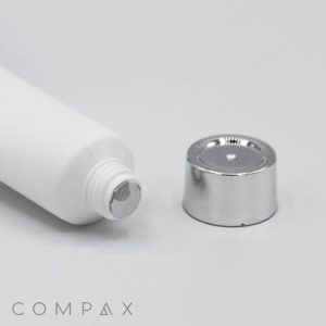 A close-up of a white 19mm Screw Top tube with its metallic cap removed. The tube lies horizontally on a white surface with the cap placed beside it, revealing the threaded opening. The brand "COMPAX" is seen in the bottom-left corner.