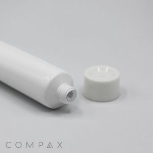 A white, cylindrical "22mm Screw Top" tube with its cap off, placed on a white surface. The threading and opening of the tube are visible, and the cap is positioned to the right of the tube. The brand name "COMPAX" is printed in gray at the bottom left corner.