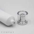 The image depicts a white cylindrical cosmetic bottle lying on its side, with its clear, silver-colored 25mm Screw Top cap removed and placed next to it. The cap features a transparent outer layer and a reflective interior. The word "COMPAX" is visible in light gray text in the bottom left corner.