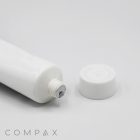 A close-up of an opened 25mm Screw Top with a threaded end, shown lying horizontally on a white surface. The white screw-on cap is placed next to the tube. The word "COMPAX" is printed in the bottom-left corner.