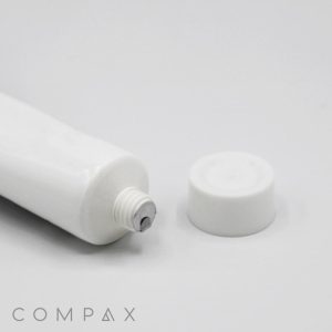 A close-up of an opened 25mm Screw Top with a threaded end, shown lying horizontally on a white surface. The white screw-on cap is placed next to the tube. The word "COMPAX" is printed in the bottom-left corner.