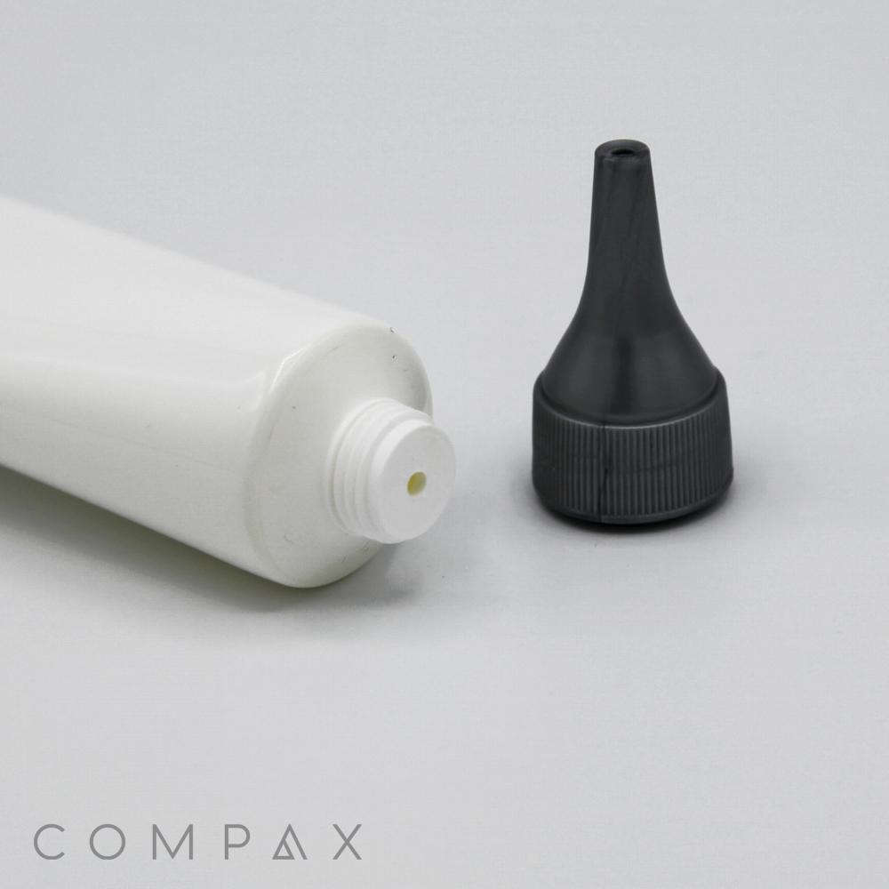A close-up image of an open 30mm Needle Nose Twist tube with its gray cap removed, placed on a flat light gray surface. The gray cap features a precision spout for controlled dispensing. The brand name "COMPAX" is visible in the bottom left corner of the image.