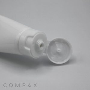 A close-up image of a white plastic squeeze tube with an open 30mm Flip Top cap. The nozzle is visible, and a small amount of the product may be seen, indicating it is ready for use. The word "COMPAX" is written in the bottom left corner.
