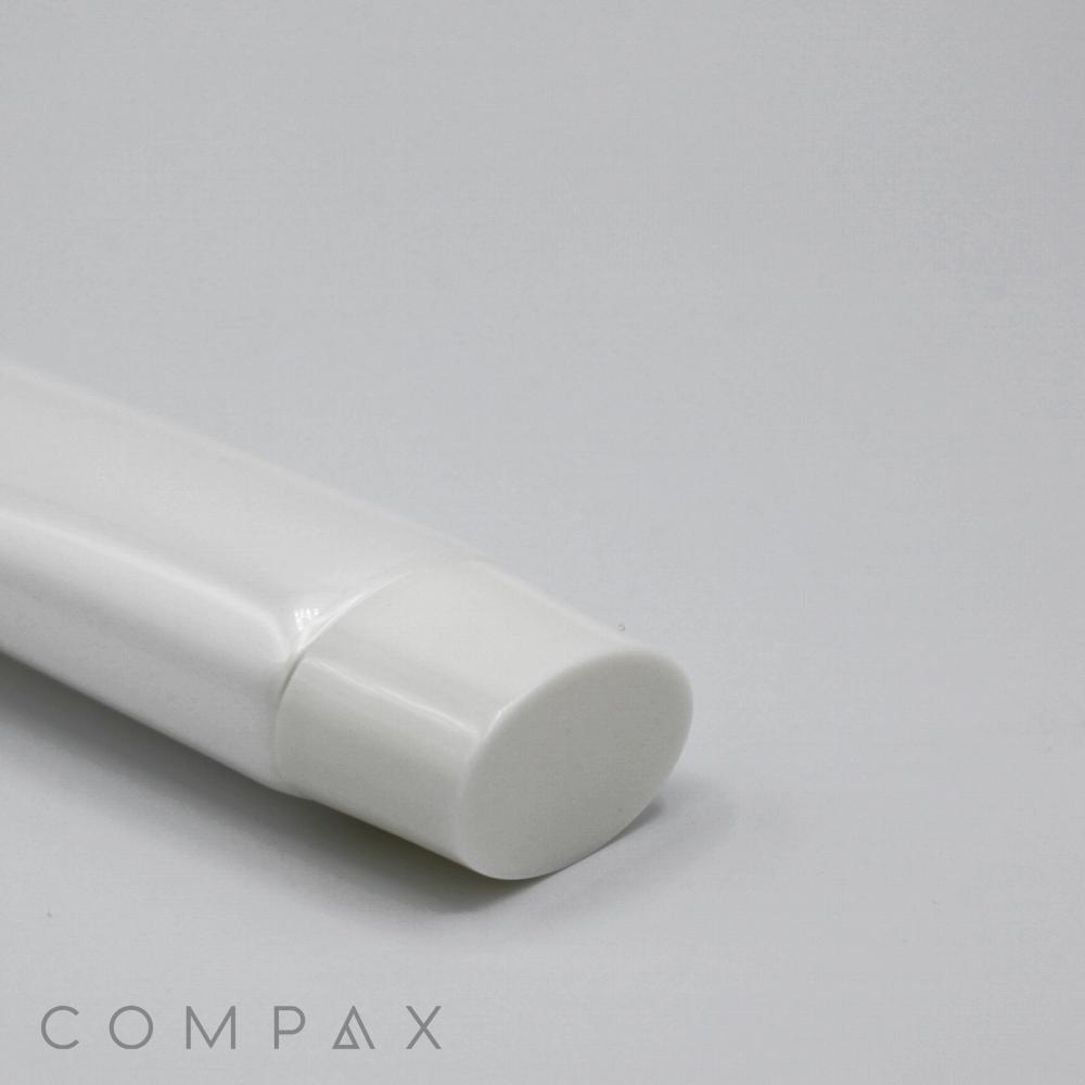 A close-up of a white plastic tube labeled "30mm Flat Screw Top" with a white cap lying on a light gray surface. The text "COMPAX" is visible in the bottom-left corner.