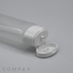 A 30mm Oval Flip Top clear plastic bottle with a white flip-top cap is shown lying on its side. The cap is open, revealing the nozzle for dispensing the bottle's contents. The brand name "COMPAX" is printed in the bottom left corner of the image.