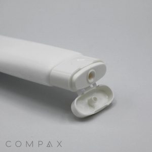 A white, cylindrical plastic tube labeled "35mm Flat Flip Top" is open, showcasing its dispensing nozzle. The background is plain light grey. The word "COMPAX" is visible in light grey letters in the bottom left corner.