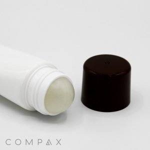 A white plastic tube with a smooth, rounded roller ball applicator lies on its side next to a black, cylindrical cap. The word "COMPAX" is written in small grey letters at the bottom left corner of the image. The background is white and seamless.