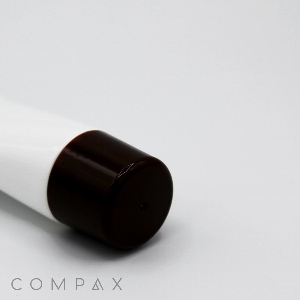 A close-up image of a white 35mm Roller Ball cosmetic tube with a dark brown cap, lying on its side. The word "COMPAX" is printed in light gray capital letters at the bottom left corner of the image against a light gray background.
