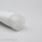 An up-close image of a white tube with a transparent cap, placed on a plain white background. The brand name "COMPAX" is visible in the bottom left corner. The tube, labeled as "38mm Flip Top," appears to be a cosmetic or skincare product.