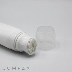 A 40mm Silicone Brush Applicator featuring a white cylindrical tube with a textured, bristled applicator tip is shown lying on a white surface. The transparent cap is off and placed next to the tube, with the word "COMPAX" displayed in the bottom left corner.