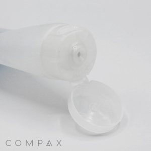 A 40mm Flip Top open, translucent white plastic squeeze bottle lies on its side with its flip-top cap open, revealing a small dispenser nozzle. The word "COMPAX" is printed in gray at the bottom left corner. The background is white.