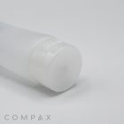 A close-up of a semi-transparent, cylindrical plastic bottle with a white cap lying horizontally on a white surface. The cosmetic bottle, named "40mm Flip Top," features minimal branding with "COMPAX" written in light gray text at the bottom left corner.