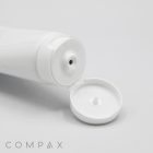 A close-up image of an open white 40mm Flip Top squeeze tube with a wide flip-top lid. The tube is positioned horizontally, and the small dispensing hole is visible. The brand name "COMPAX" is printed in subtle, light grey letters at the bottom left corner.