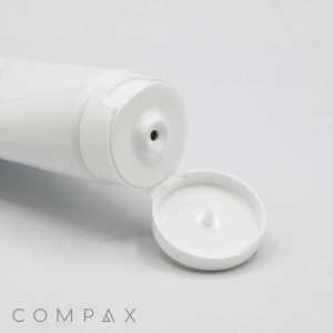 A close-up image of an open white 40mm Flip Top squeeze tube with a wide flip-top lid. The tube is positioned horizontally, and the small dispensing hole is visible. The brand name "COMPAX" is printed in subtle, light grey letters at the bottom left corner.
