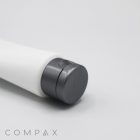 A white cylindrical tube labeled "40mm Flip Top," featuring a gray flip-top cap, is positioned horizontally on a white surface. The word "COMPAX" is printed in gray text near the bottom left corner.