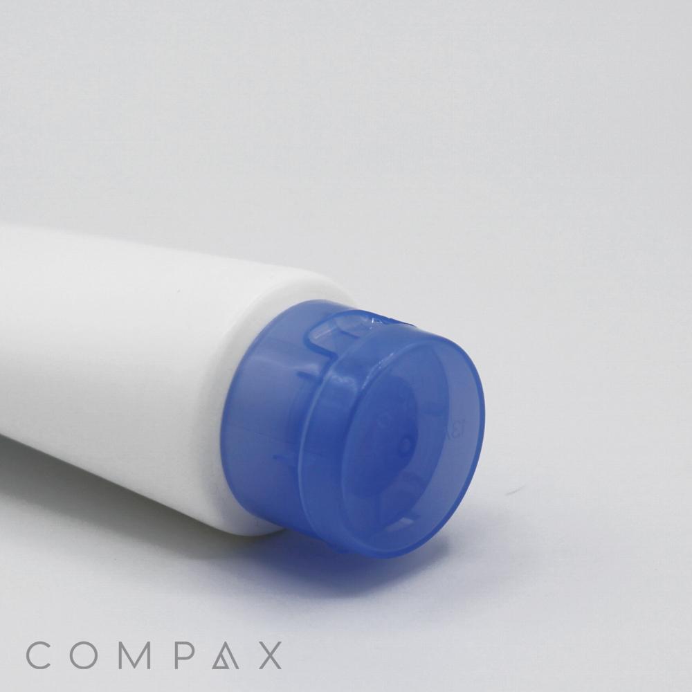 A close-up image of a white 40mm Flip Top tube with a blue flip-top cap lying on its side against a plain background. The tube has the word "COMPAX" printed near the bottom.