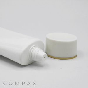 A white 40mm Oval Screw Top tube with a nozzle is shown lying on a flat surface with its cap removed and placed beside it. The cap is white with a gold trim at the bottom edge. The brand name "COMPAX" is visible in the lower-left corner. The background is plain white.