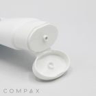A 40mm Oval Flip Top white plastic tube with a flip-open cap lies on a plain white background. The opening of the tube is visible, showing a small nozzle for dispensing the product. The word "COMPAX" is printed near the bottom left corner of the image.