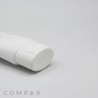 A portion of a white, cylindrical tube container with a round, flat cap is partially visible against a plain, off-white background. The word "COMPAX" is printed in light gray in the bottom left corner of the image.