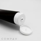 A close-up image of an open 45mm Flip Top squeeze tube with a hinged white cap. The tube is positioned at an angle, with the open cap facing the camera, revealing a small nozzle. The background is plain white, and "COMPAX" is written in gray text at the bottom left corner.