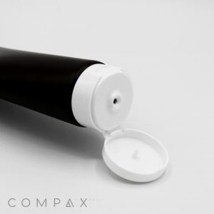 A close-up image of an open 45mm Flip Top squeeze tube with a hinged white cap. The tube is positioned at an angle, with the open cap facing the camera, revealing a small nozzle. The background is plain white, and "COMPAX" is written in gray text at the bottom left corner.
