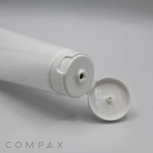 A white plastic tube from the "45mm Flip Top" product line lies on a flat surface with its flip-top cap open, revealing a small opening for dispensing contents. Both the tube and cap are white, and the plain tube surface has no visible labeling except for the word "COMPAX" written in grey in the bottom left corner.