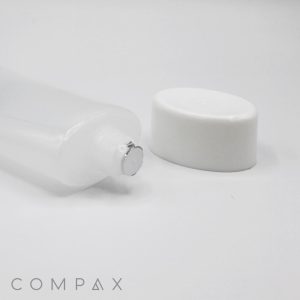 A 50mm Oval Screw Top squeezable plastic tube with a metallic seal is lying on its side, with its white cap placed nearby. The brand name "COMPAX" is visible in the lower left corner. The background is plain white.