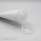 A white cylindrical tube with a clear flip-top cap lies on a flat surface, open and facing upwards. The product name "50mm Flip Top" and the brand name "COMPAX" are visible in the lower left corner. The background is plain and light grey.