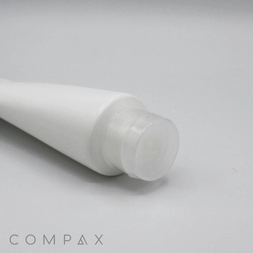 A close-up view of a white, cylindrical plastic tube labeled "50mm Flip Top," featuring a translucent cap and viewed from the side. The tube is positioned at an angle, with the word "COMPAX" visible in the bottom left corner of the image.