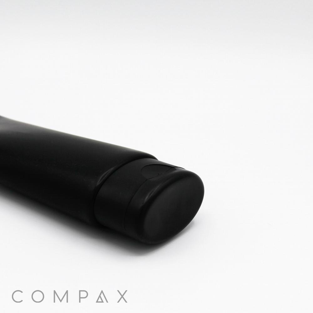 A black, 50mm oval flip top tube with a cap is placed on a white surface. The brand name "COMPAX" is visible in light gray text at the bottom left corner of the image.