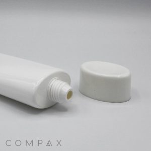 Close-up of an open 50mm Oval Screw Top tube lying horizontally, with its white cap placed separately beside the opening. The background is plain white, and "COMPAX" is written in gray text at the bottom left corner of the image.